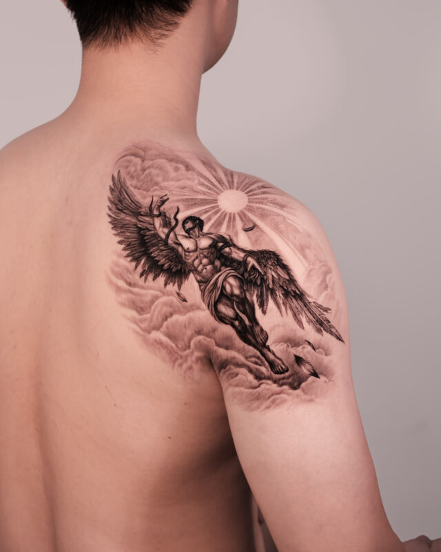 Black and grey Icarus tattoo with wings, clouds and sun across the shoulder by Azone Tattoo Studio in Hanoi