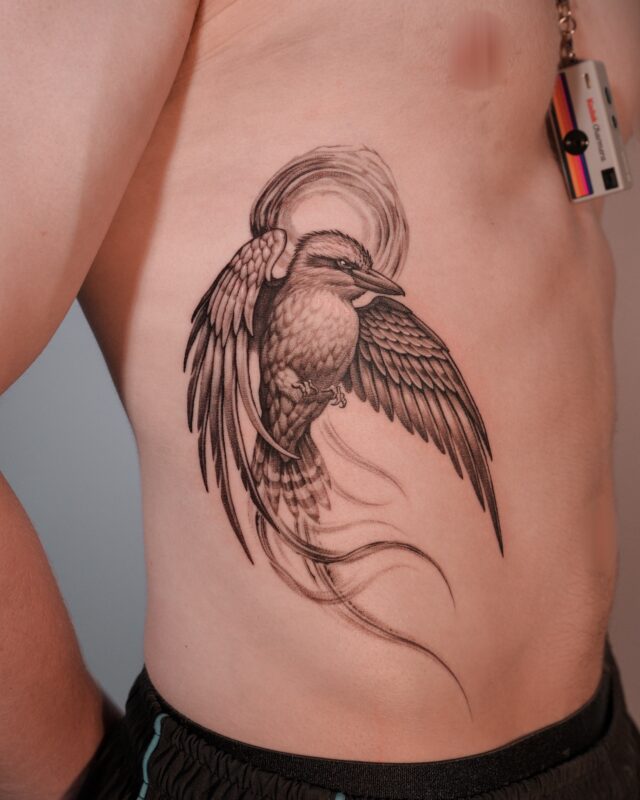 Black and grey kingfisher tattoo with flowing wing details on the side ribs by Azone Tattoo Studio in Saigon.