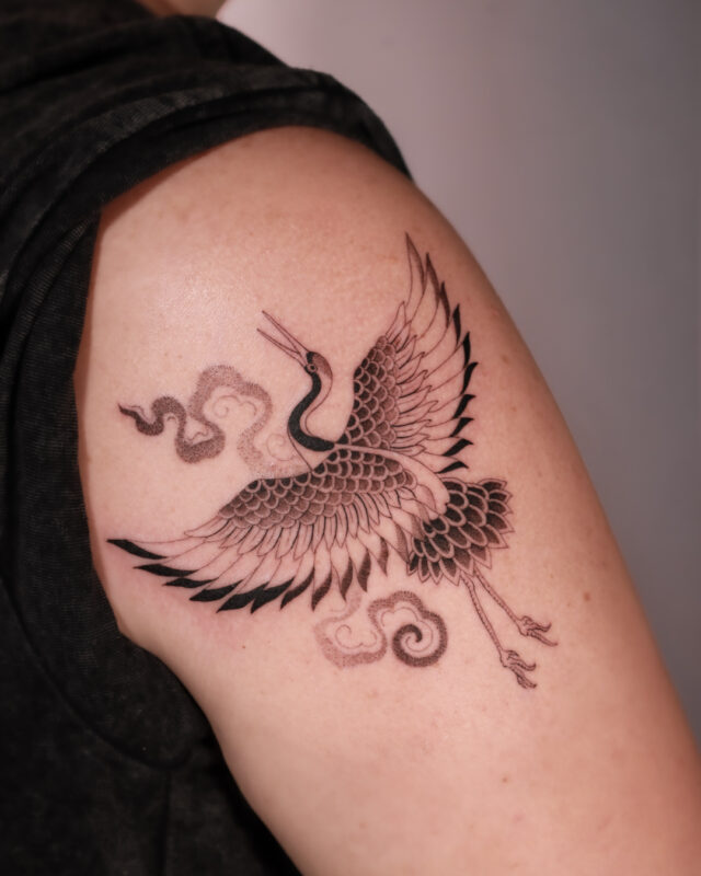 Blackwork crane tattoo with cloud details on the upper arm by Azone Tattoo Studio in Hanoi and Saigon