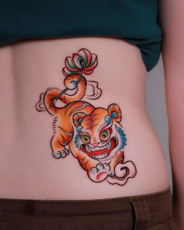 Vietnamese folk art-inspired tiger tattoo featuring a lotus flower, stylized clouds, and vibrant traditional colors on the side of the body.