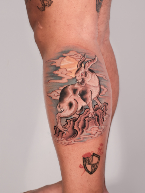 Japanese-inspired rabbit tattoo featuring a full moon, flowing clouds, and rocky elements on the leg.