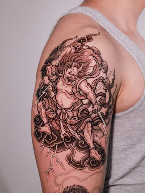 Japanese Raijin thunder god tattoo with drums, clouds and lightning on the upper arm by Azone Tattoo Studio in Hanoi